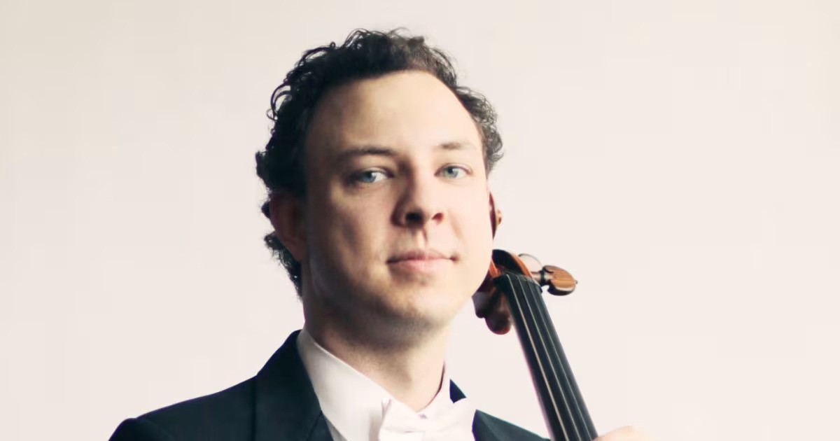 Jeremy Crosmer in a suit stands holding a cello