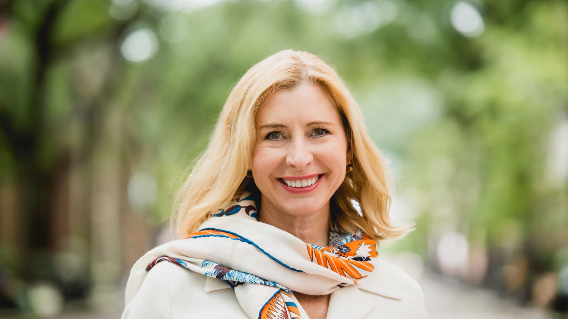 Rebecca Patterson in a white coat and scarf smiles warmly at the camera