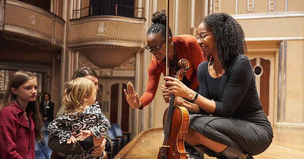 A woman plays the violin while two young girls listen attentively