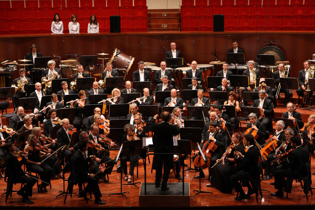 A conductor leads an orchestra performing in a spacious auditorium